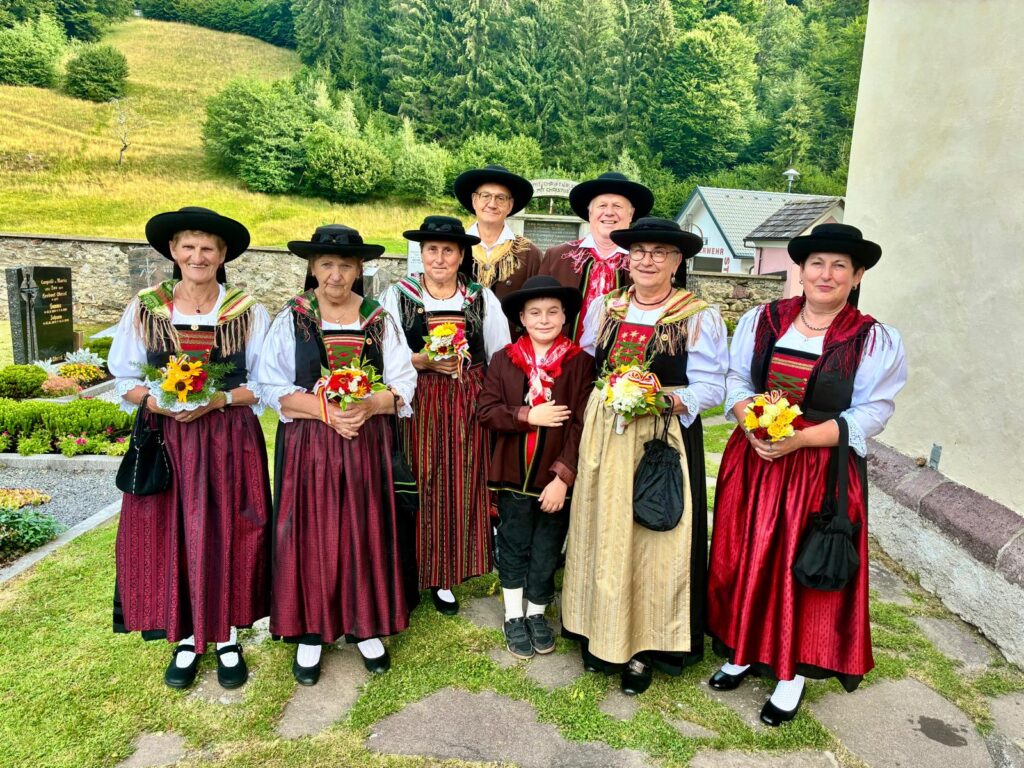 Trachtengruppe mit Blumensträußen vor Kirche in einem Bergdorf